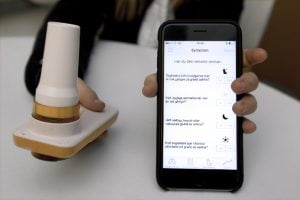 Händer håller en mobil med appen asthmatuner och ett munstycke
