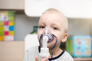 Liten pojke inhalerar astmamedicin med andningsmask