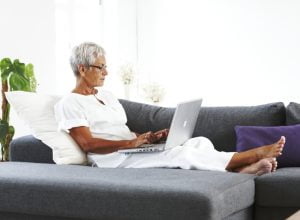 Äldre kvinna tittar på laptop liggande i soffa