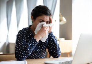 Kvinna nyser i näsduk framför datorn
