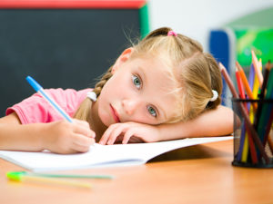 Trött liten flicka vilar huvudet mot skolbänken