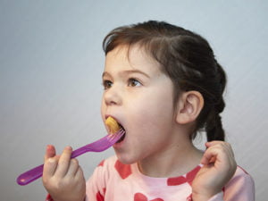 Flickan Alba stoppar in en jordnötsbåge i munnen med gaffel