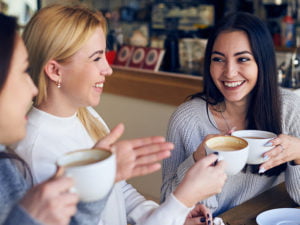 Tre unga kvinnor med kaffekoppar på kafé