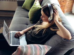 Ung kvinna i soffa med hörlurar på huvudet och laptop i knät