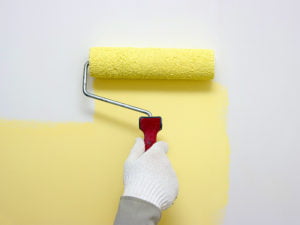 Hand med roller målar vit vägg med gul färg